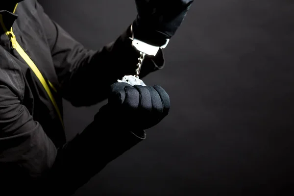 Close-up das mãos de um ladrão em luvas pretas com algemas em um fundo preto — Fotografia de Stock