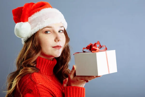 Belle dame en chapeau Santa tient des cadeaux, regardant la caméra et souriant, isolé sur fond gris — Photo