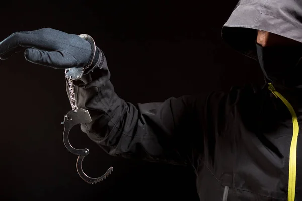 Крупный план рук грабителя в черных перчатках с наручниками на черном фоне — стоковое фото