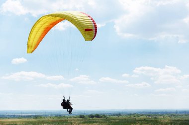 Sarı Paraglider, güneşli bir günde bulutlarla gökyüzüne uçuyor..