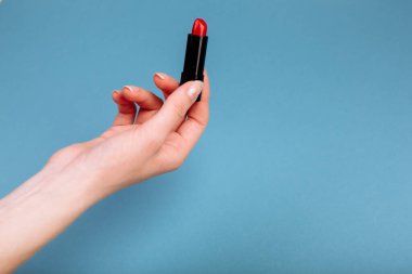 Kadın eli kırmızı ruj alıyor. Mavi arkaplanda izole edilmiş