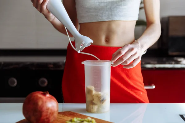 Woman with hand blender making sweet banana protein milkshake. sport nutrition diet after gym. Healthy lifestyle