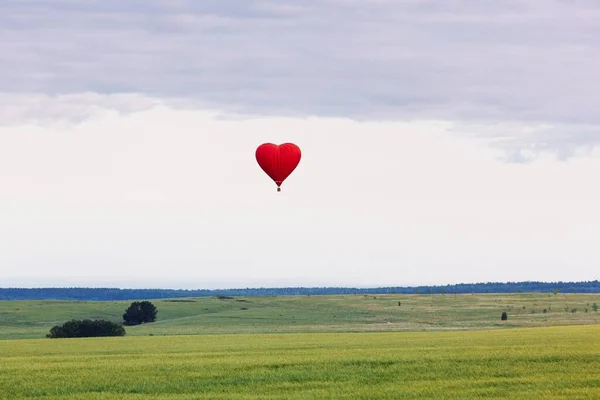 Red hot air balloon in shape of heart is landing on the green field — Stock Photo, Image