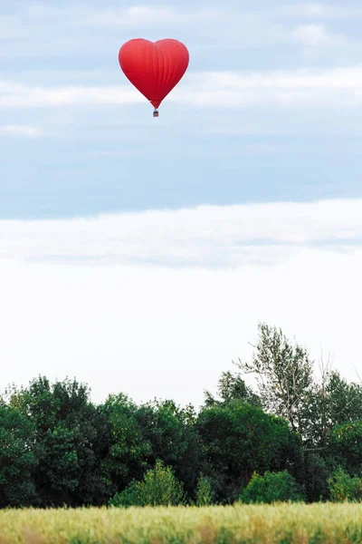 Red hot air balloon in shape of heart is landing on the green field — Stock Photo, Image