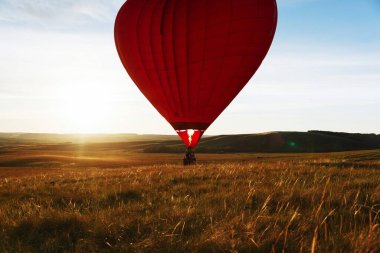 Sıcak kırmızı hava balonu kalp şekli vadi üzerinde gün batımına doğru uçuyor ya da kalkıyor.