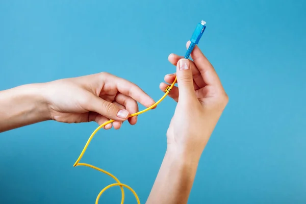 Las manos de las mujeres sostienen SC y FC conector cable de conexión de fibra óptica monomodo sobre fondo azul Imagen de stock