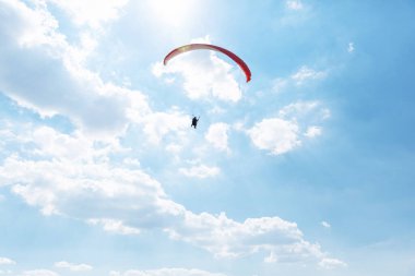 Sarı Paraglider tandem eğitmeni, güneşli bir günde bulutlarla gökyüzüne uçan bir turist..