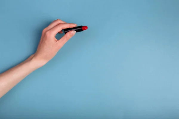 La mano de las mujeres está tomando lápiz labial rojo. aislado En el fondo azul Imagen de archivo