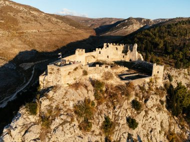 Gün batımında, engebeli dağlar ve orman vadisiyle çevrili kayalık bir tepedeki Ljubushki Kalesi 'nin hava manzarası. g.