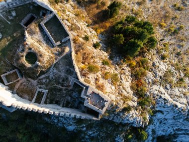 Gün batımında, engebeli dağlar ve orman vadisiyle çevrili kayalık bir tepedeki Ljubushki Kalesi 'nin hava manzarası. g.