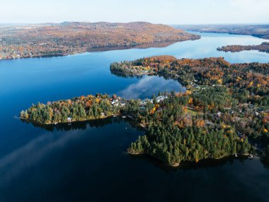 Kanada 'da yerleşim binaları ve sonbahar ormanları olan dolambaçlı bir göl yolu insansız hava aracı. g.