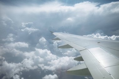 Beyaz kabarık bulutların ve mavi gökyüzünün üzerinde kanatları olan uçak penceresinden bak.