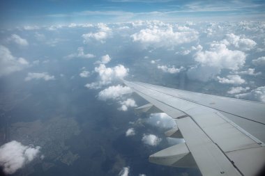 Beyaz kabarık bulutların ve mavi gökyüzünün üzerinde kanatları olan uçak penceresinden bak.
