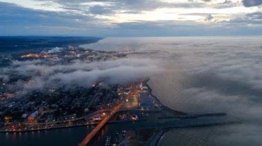Nehir, sis, alçak bulutlar ve Kanada 'nın Quebec kenti boyunca uzanan şehir ışıklarıyla Matane şehrinin hava manzarası. g.