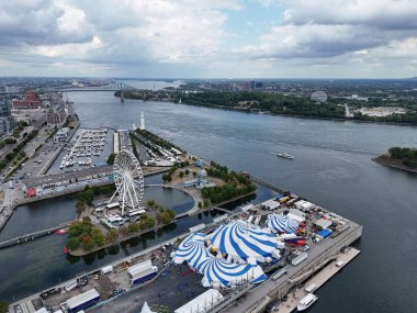 24 Ağustos 2025 Monreal Eski Limanı 'ndaki Cirque du Soleil mavi-beyaz çadırında arka planda şehir silueti olan insansız hava aracı uçuşu. g.