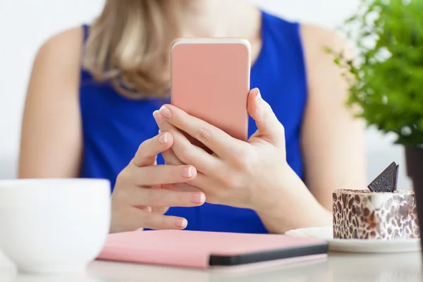 Vrouw in blauwe jurk in het café houden van roze telefoon — Stockfoto
