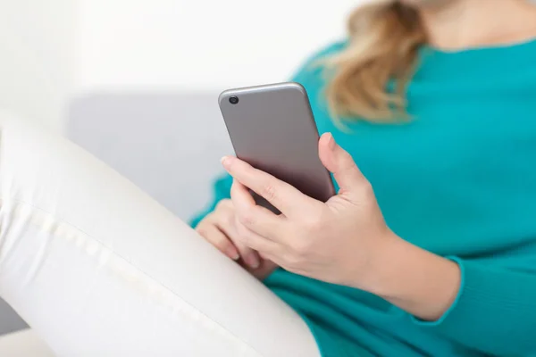 Mulher sentada no sofá e segurando um telefone celular — Fotografia de Stock