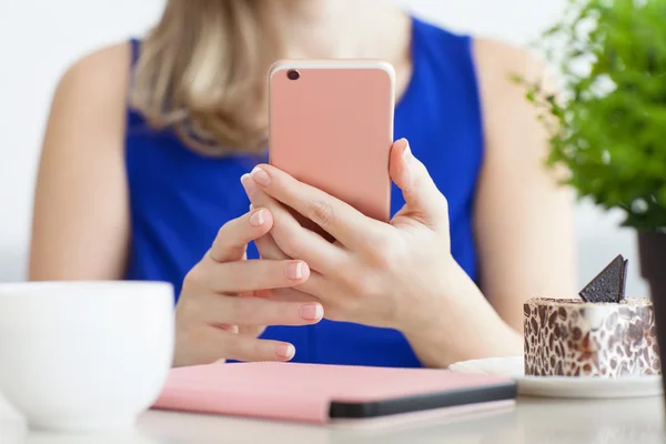 Kvinna i blå klänning i kaféet håller rosa telefon — Stockfoto