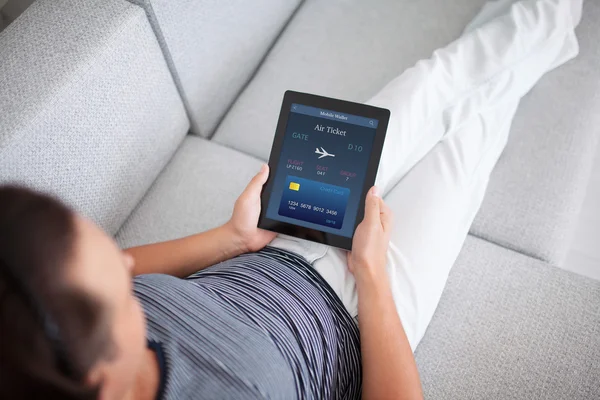 Man on sofa holding tablet computer with online air ticket — Stock Photo, Image