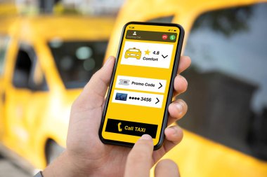 Adam, sarı arabaların arka planında telefonla taksi çağırma uygulamasını ekranda tutuyor