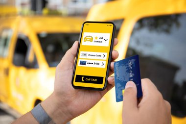 Adam telefonu ekranda taksi çağırma başvurusu ve sarı arabaların arka planında plastik kartla tutuyor.