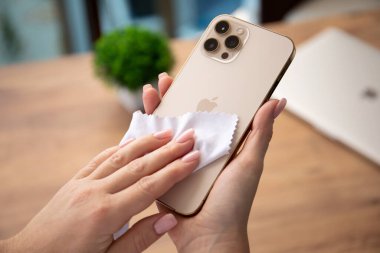 Alanya, Türkiye - 26 Kasım 2020: Apple iPhone 12 Pro Max Gold 'u tutan ve onu paçavrayla ovuşturan kadın. iPhone Apple tarafından oluşturuldu ve geliştirildi..