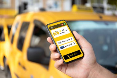 Adam, sarı arabaların arka planında telefonla taksi çağırma uygulamasını ekranda tutuyor