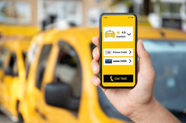 Adam, sarı arabaların arka planında telefonla taksi çağırma uygulamasını ekranda tutuyor