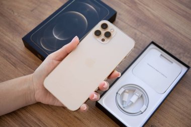 Alanya, Türkiye - 26 Kasım 2020: Apple iPhone 12 Pro Max Gold 'u tutan ve masada oturan kadın. iPhone Apple tarafından oluşturuldu ve geliştirildi..