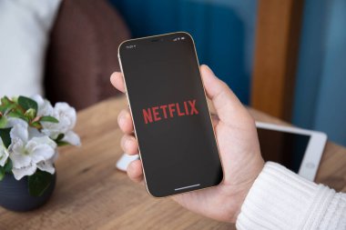 Alanya, Türkiye - 30 Mart 2021: iPhone 12 Pro Max Gold 'u çok uluslu eğlence şirketi Netflix ile elinde tutan adam ekranda yayın yapan medya ve video sunuyor.