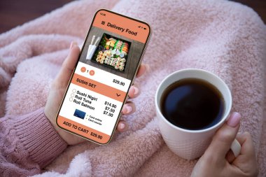 Kadın elleri, ekranda yemek teslimatı uygulaması olan bir fincan kahve tutuyor. 