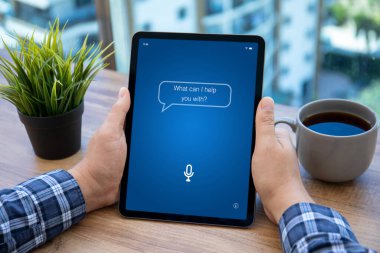 Erkek eller bilgisayar tabletini ayakta tutarken uygulama kişisel asistanı ofisteki masanın üzerinde ekranda 