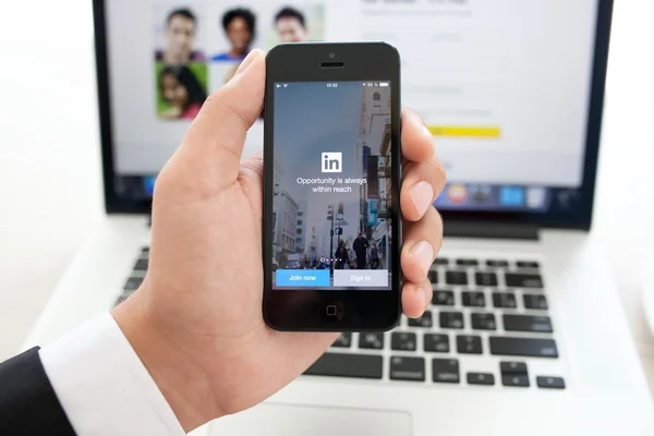 Businessman holding iPhone with app LinkedIn on the screen on a — Stock Photo, Image