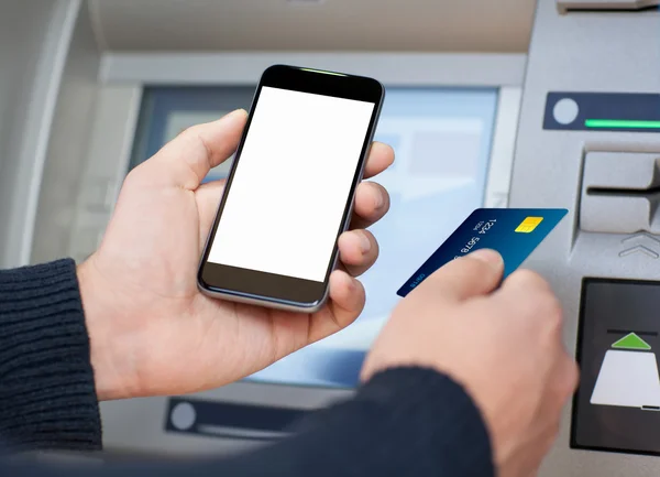 Man holding phone and a credit card at an ATM — Stock Photo, Image