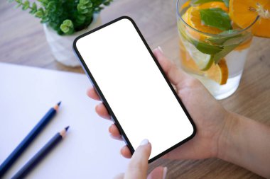 Kadın telefonu elinde tutuyor. Masanın arka planında limonata ve kafede kalemler var.