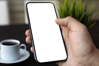 Kafe ofisinde kahve fincanı ve masasının üzerinde izole bir ekranı olan erkek el ele tutuşan telefon.