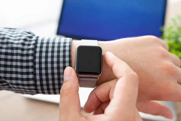 Mann hält eine Armbanduhr auf dem Hintergrund des Laptops — Stockfoto