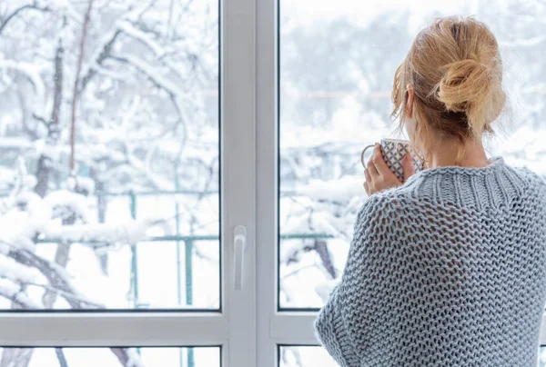 Une femme regarde par la fenêtre à l'extérieur couvert de neige — Photo