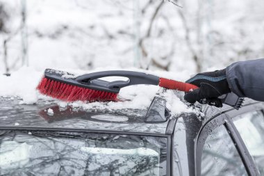 A man cleans his car from snow with a brush
