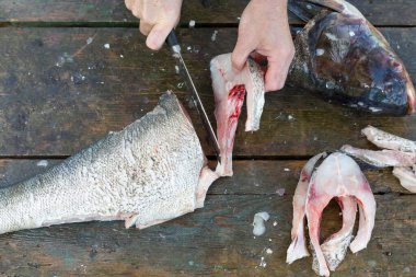Bir adam ahşap bir masada balık keser.
