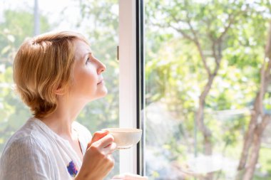 Resimli pencerede elinde çay olan bir kadın.