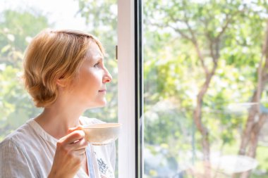 Resimli pencerede elinde çay olan bir kadın.