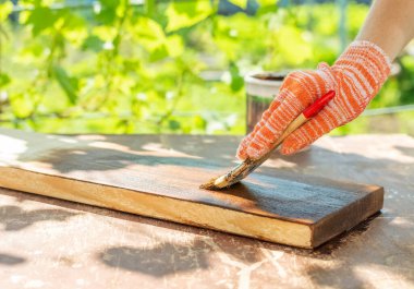 A woman in work gloves covers a board with decorative impregnation
