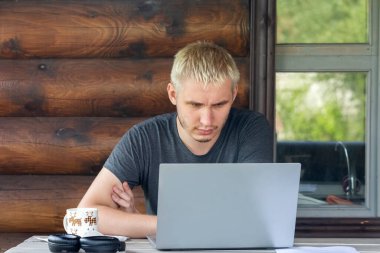 The guy is concentrating on working with a laptop, sitting on the terrace of a country house clipart