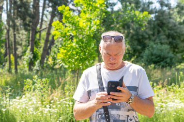 Doğada akıllı telefon kullanan yaşlı bir adam.