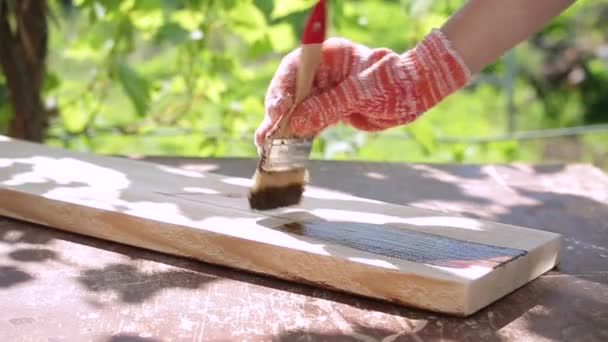 Una mano de mujer en un guante de trabajo pinta el tablero con una impregnación protectora — Vídeos de Stock