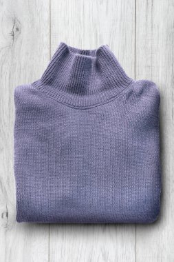 Beyaz ahşap arka planda katlanmış mor yün kazak.