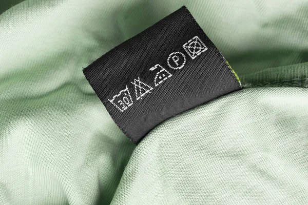 緑のテキスタイルの背景にケアの指示服ラベル — ストック写真