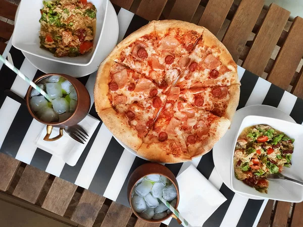 Pepperoni pizza with salad and ice lemonade on wood table