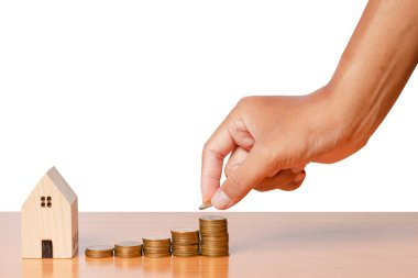 Para biriktirip beyaz arka planda izole edilmiş ahşap ev modeliyle madeni paralar koyuyorum. kırpma yolları.